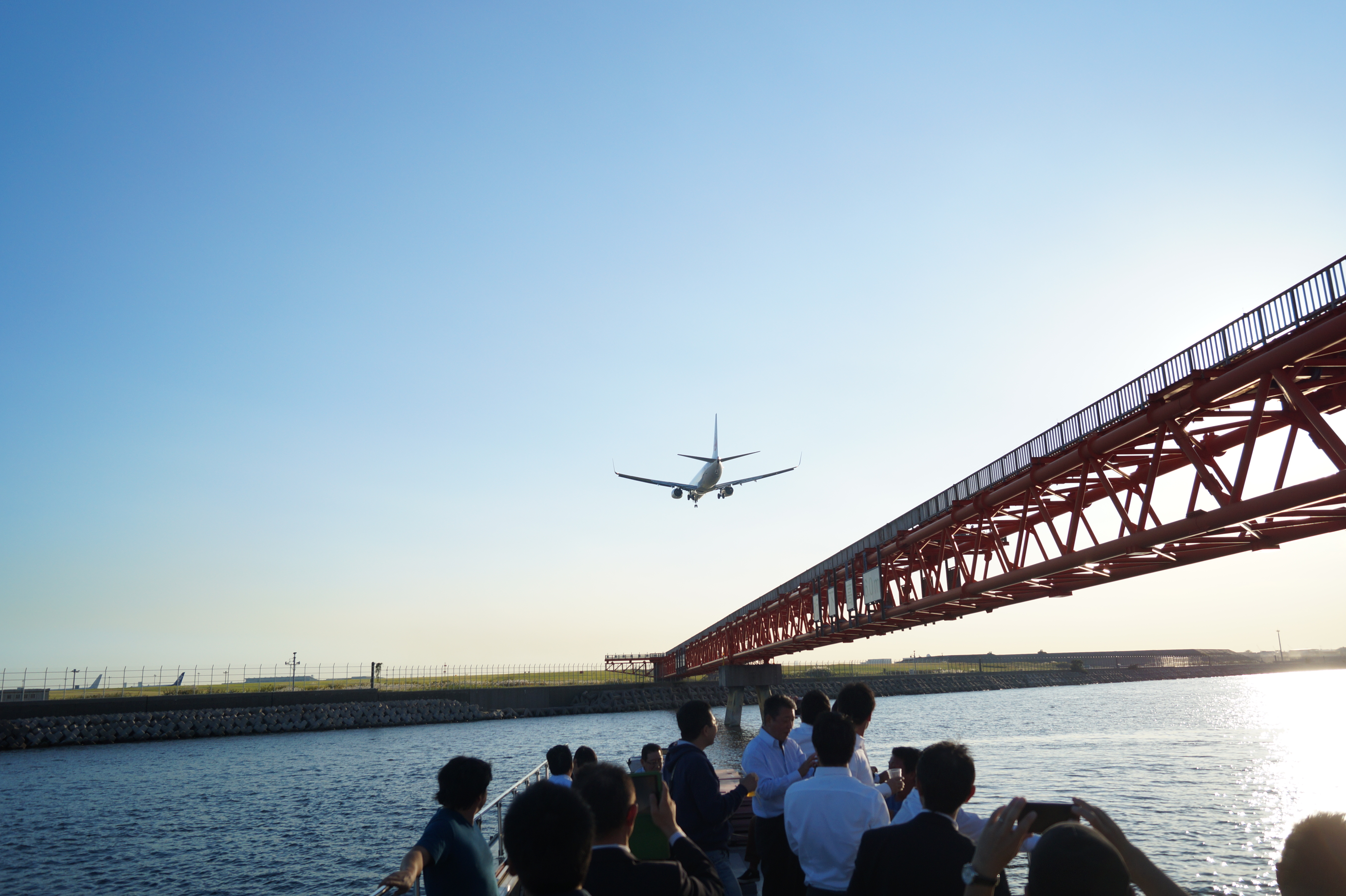 上空の飛行機を船のデッキから見上げる人々