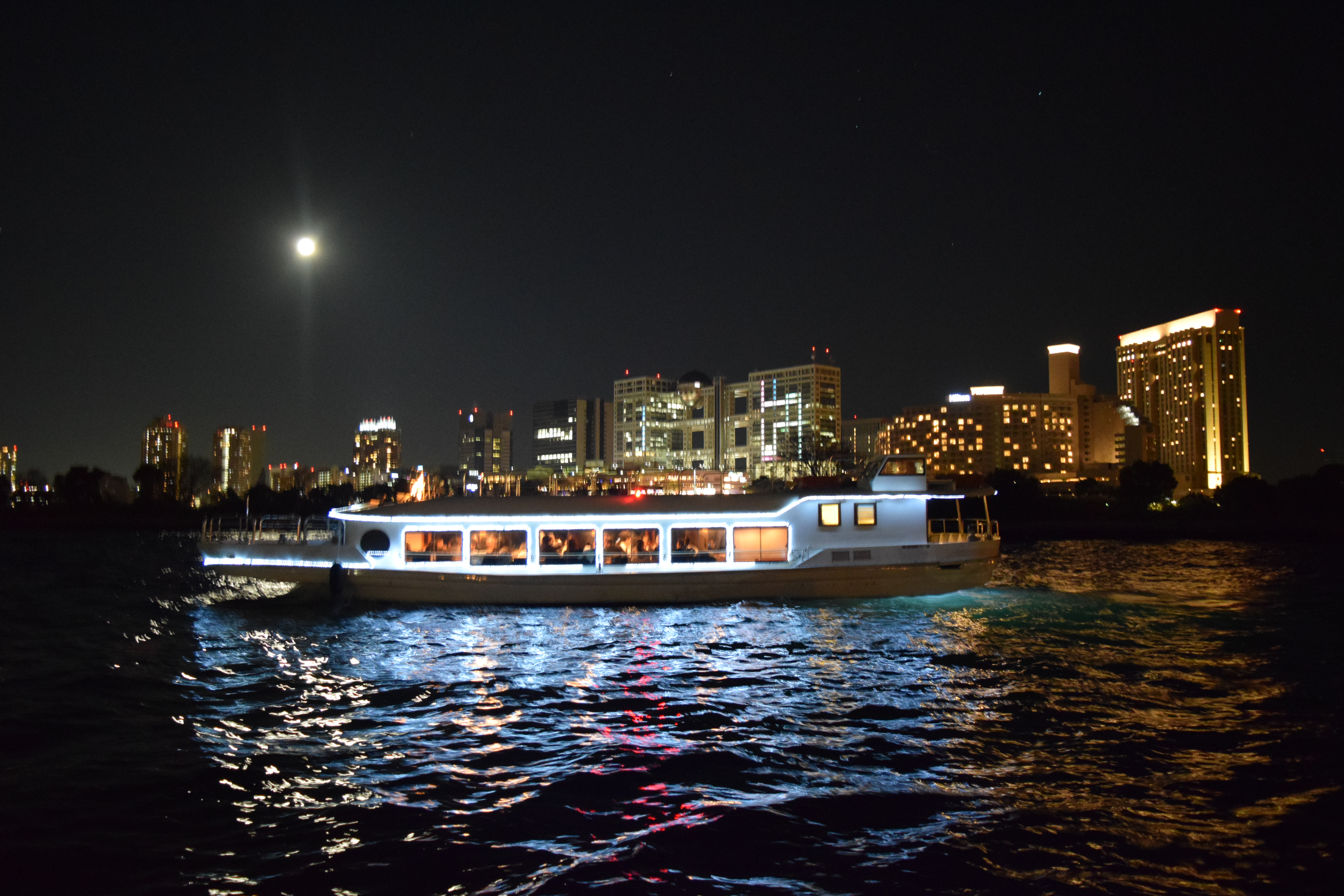 夜景をバックに月明りに照らされて海に停泊するクルーザー