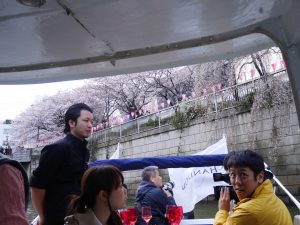 クルーザーのデッキから桜の写真を撮ろうとしている男性