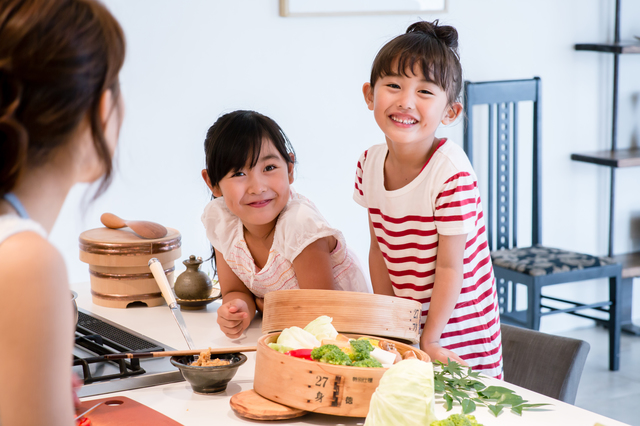 料理をするお母さんに話しかける2人の女の子