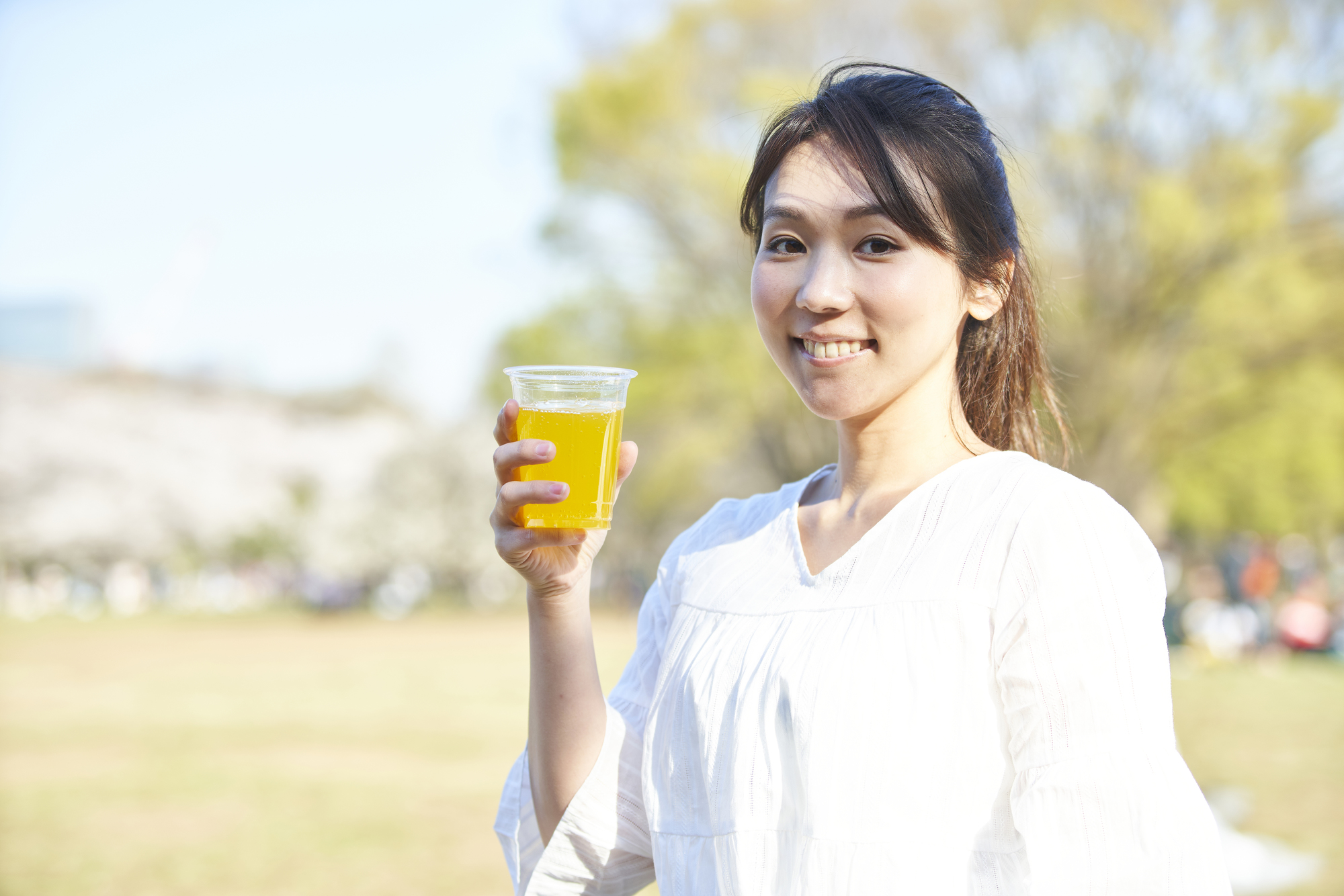 公園の緑を背景に飲み物を持つ笑顔の女性