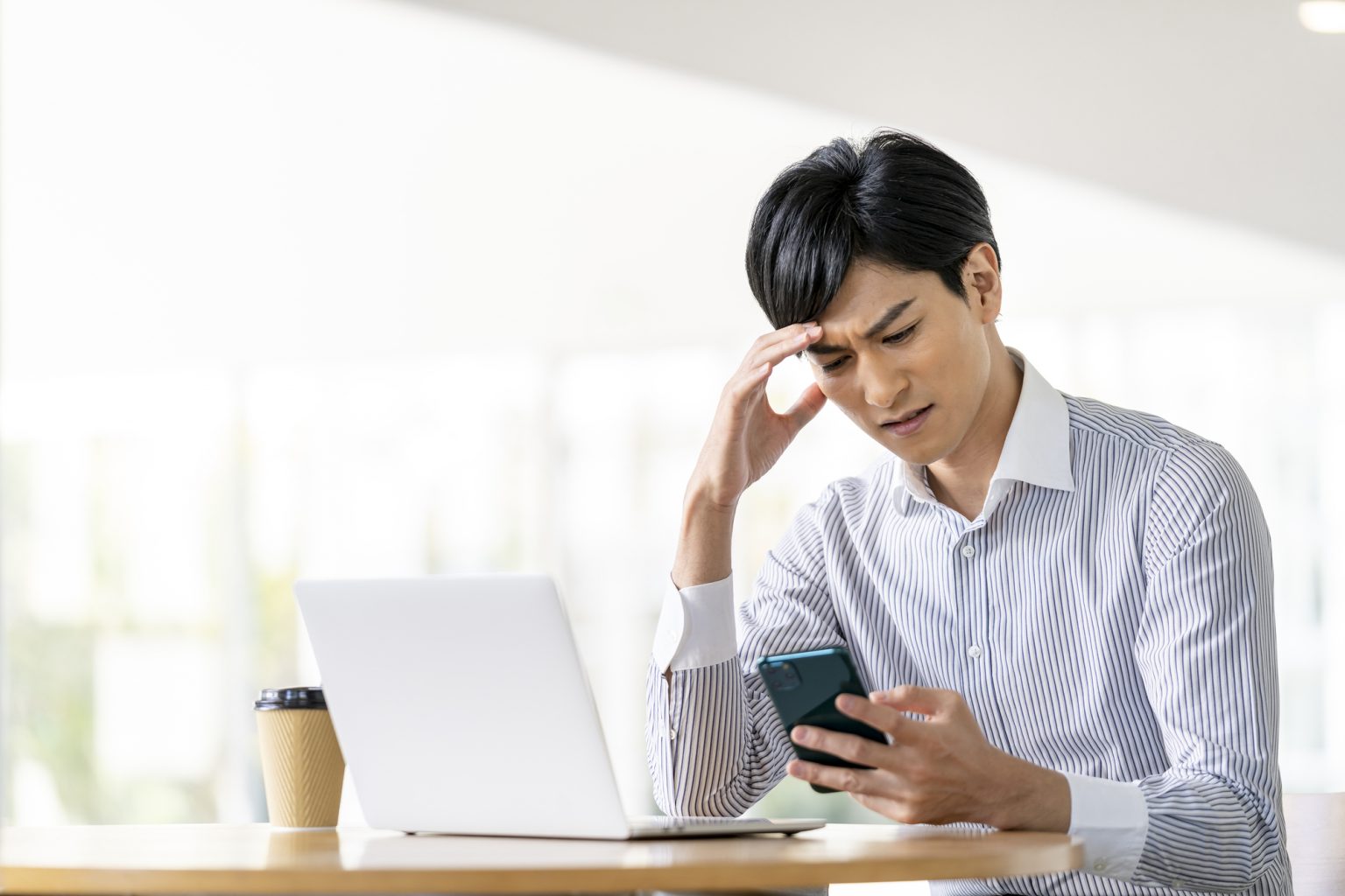 パソコンとスマホを見ながら悩む男性