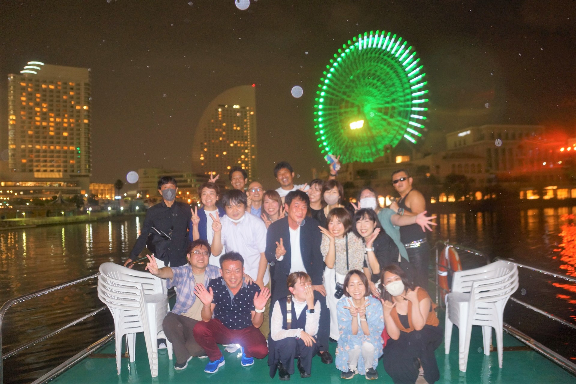 横浜の夜景を背景にし、オリエンタル号のデッキで集合写真を撮影する会社のチームメンバー