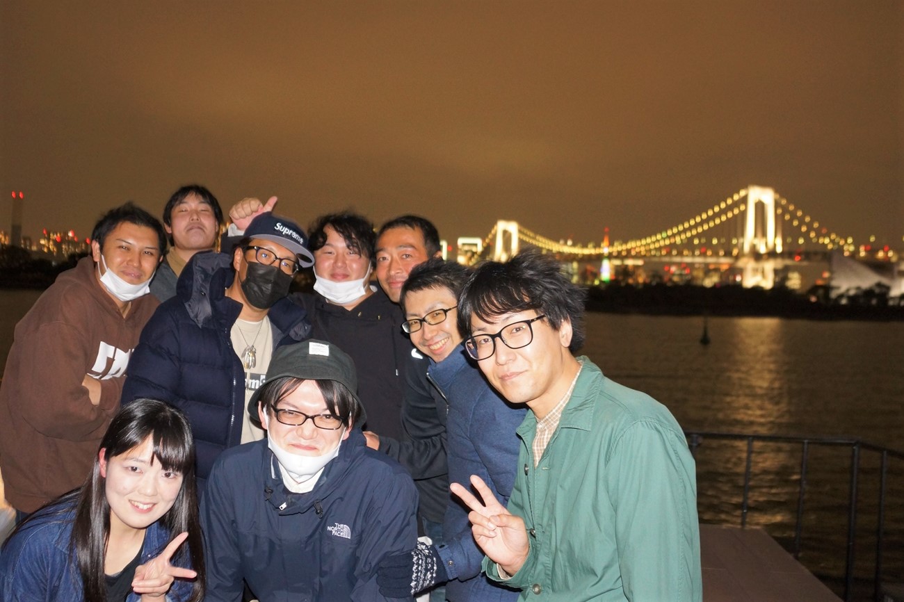 イルミネーションが点灯したレインボーブリッジを背景にグループ写真を撮影