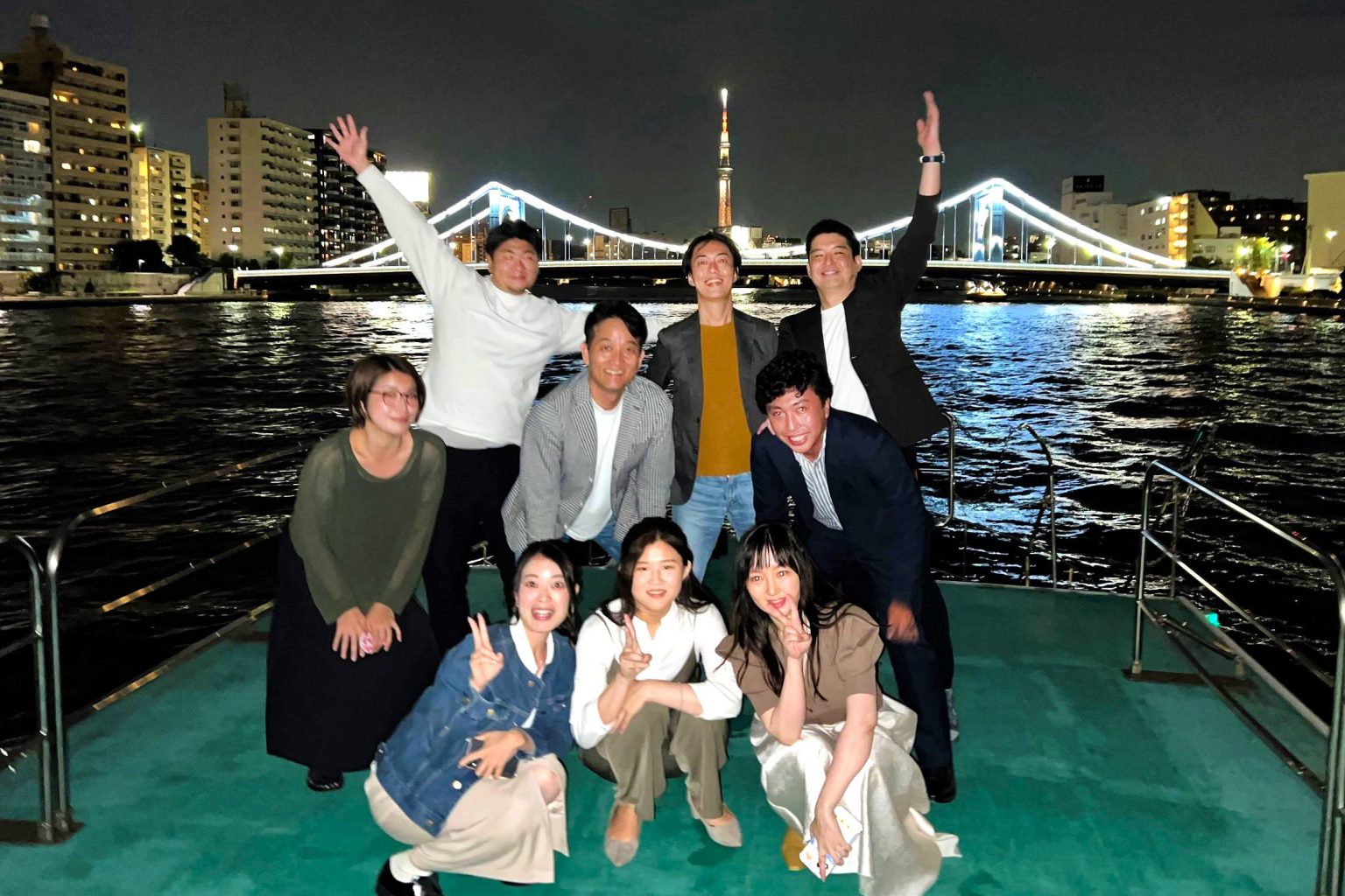 隅田川の清洲橋とスカイツリーを背景に記念撮影をする男女グループ