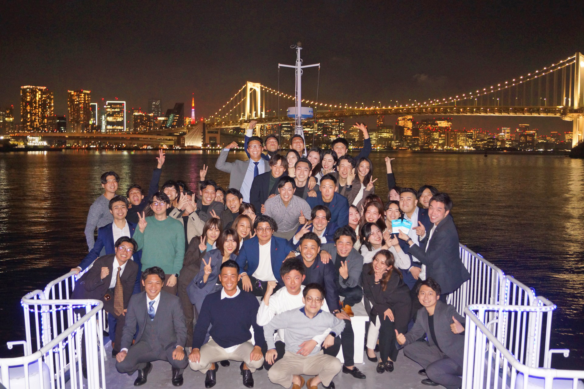 ルーカス号のデッキで集合写真を撮影する。背景にはレインボーブリッジなど東京湾の夜景が広がる。