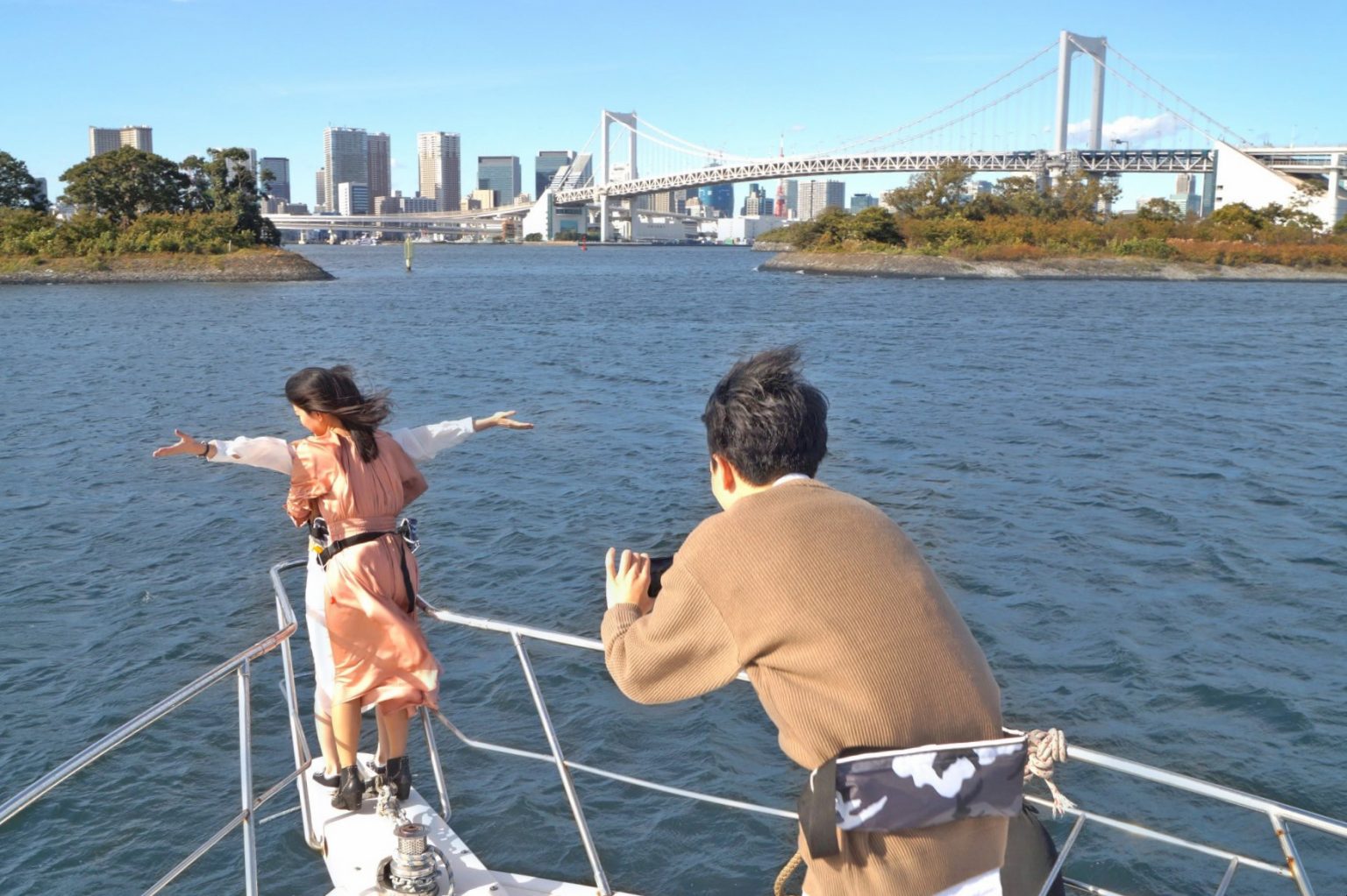 船首でタイタニックポーズをしてクルーズを楽しむ女性、を撮影する男性