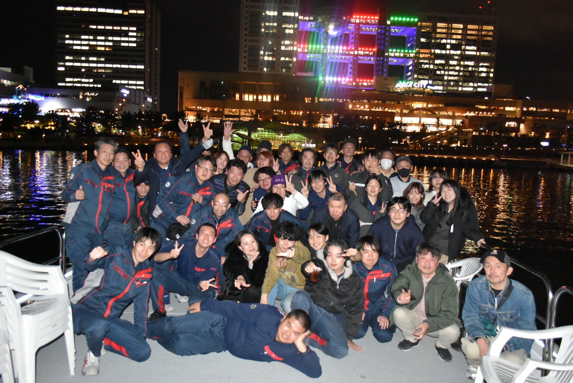 忘年会クルーズでフジテレビの夜景背景に集合写真を撮る様子